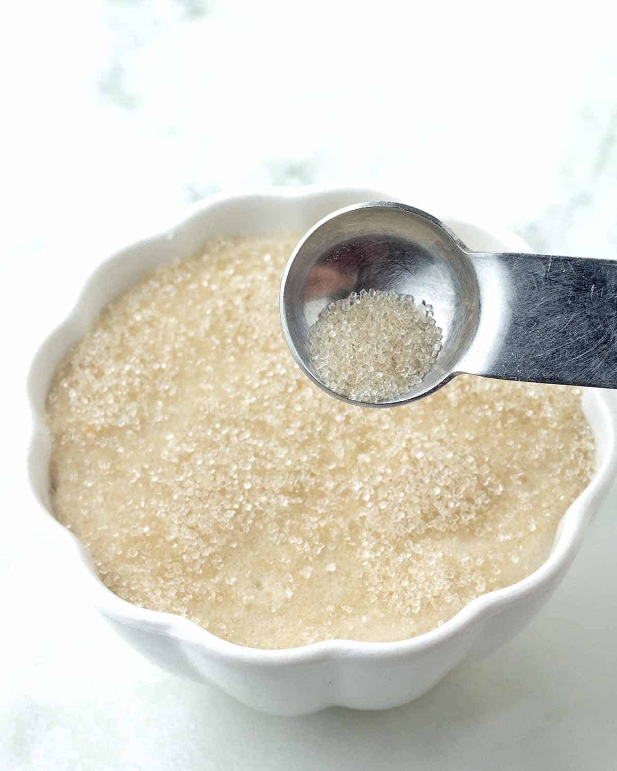 A metal measuring spoon sprinkling sugar on top of vanilla custard for vegan crème brulee.