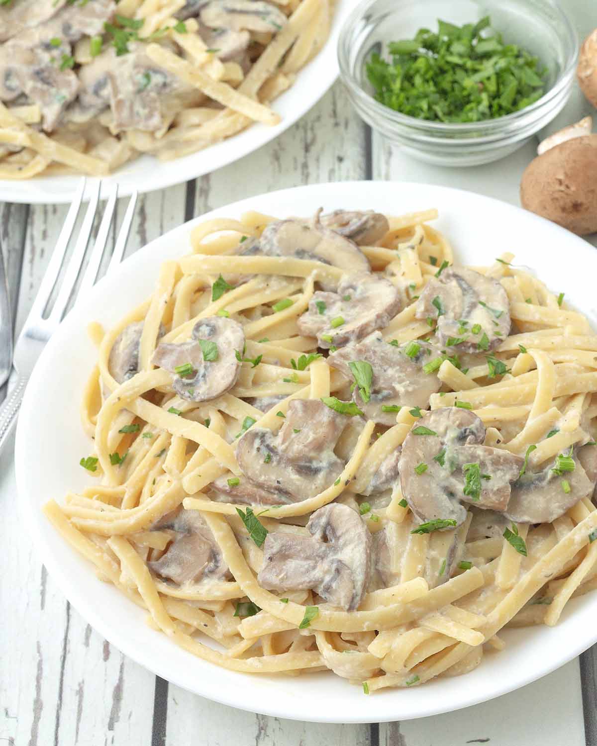 A white plate of creamy mushroom pasta garnished with chopped parsley.