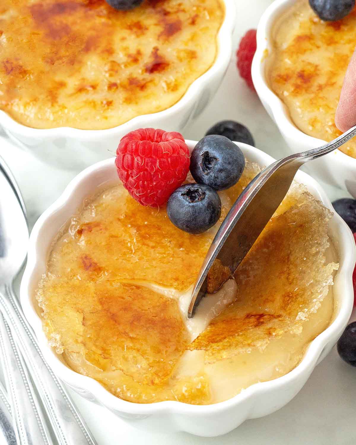 A close up shot of vegan crème brulee, a spoon is cracking the caramelized sugar shell.