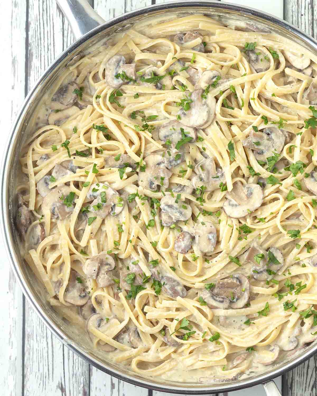 A large stainless-steel pan of freshly made vegan mushroom pasta, the pasta is garnished with fresh parsley.