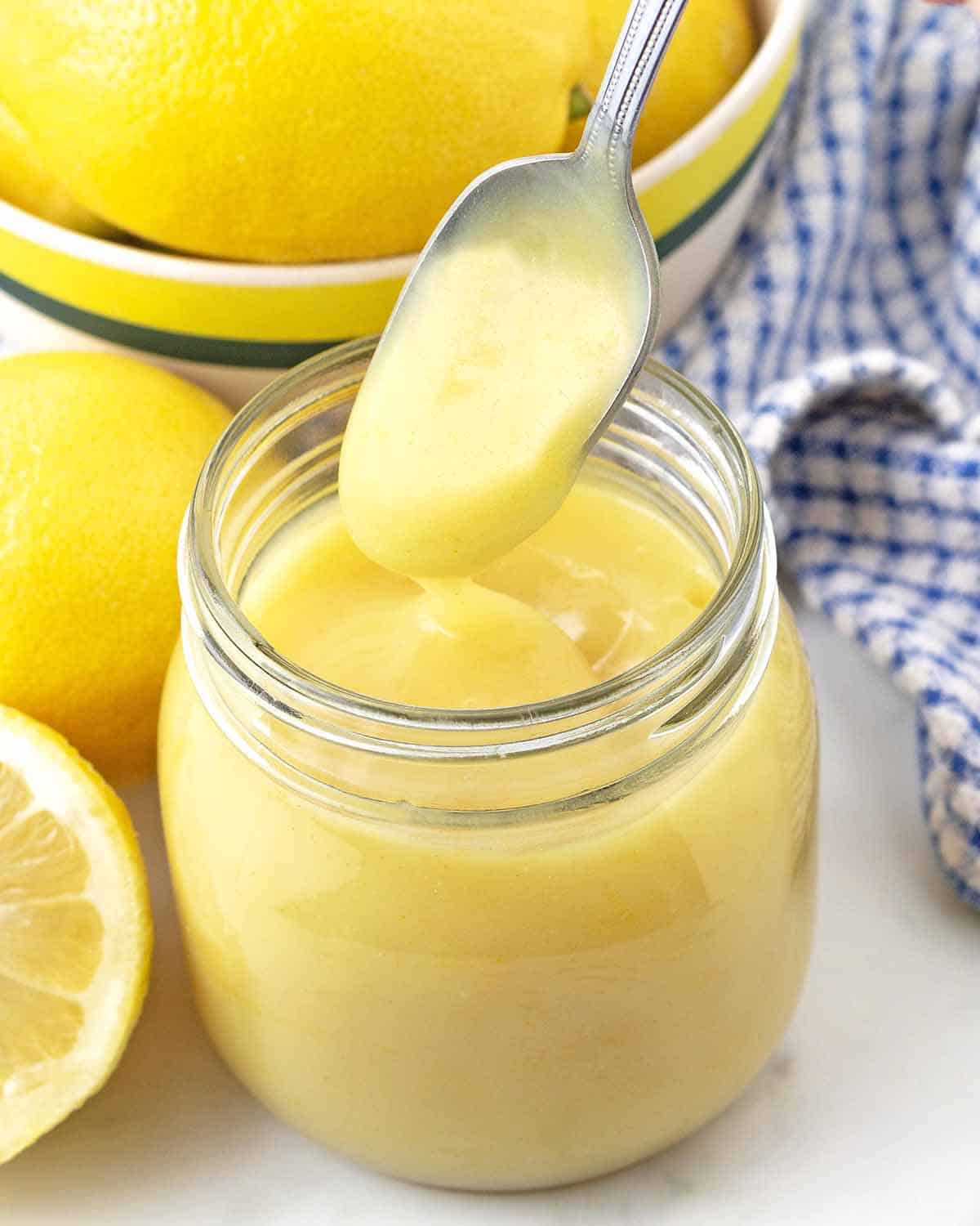 A small spoon that was just dipped into a jar of eggless lemon curd being pulled out of the jar.