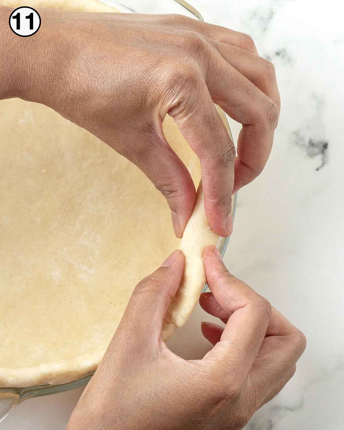 Hands folding raw pie dough overhang back to create thicker edges.