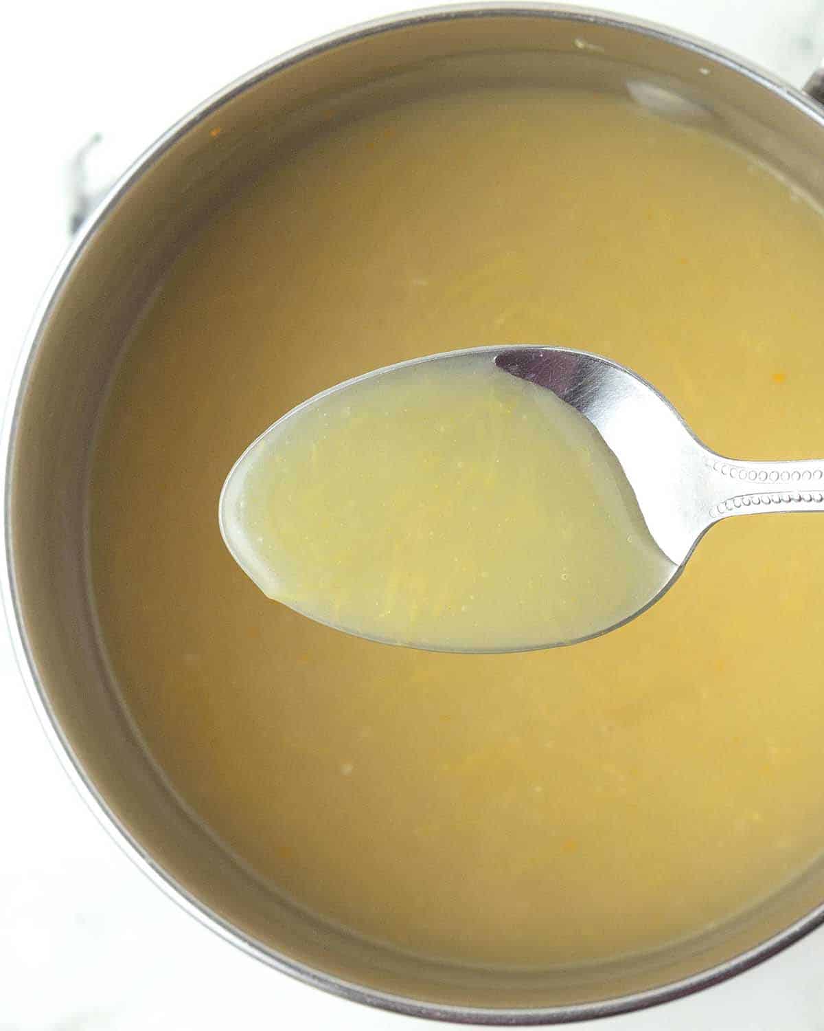 A spoon holding a small amount of almost finished vegan lemon curd to show the yellow colour.
