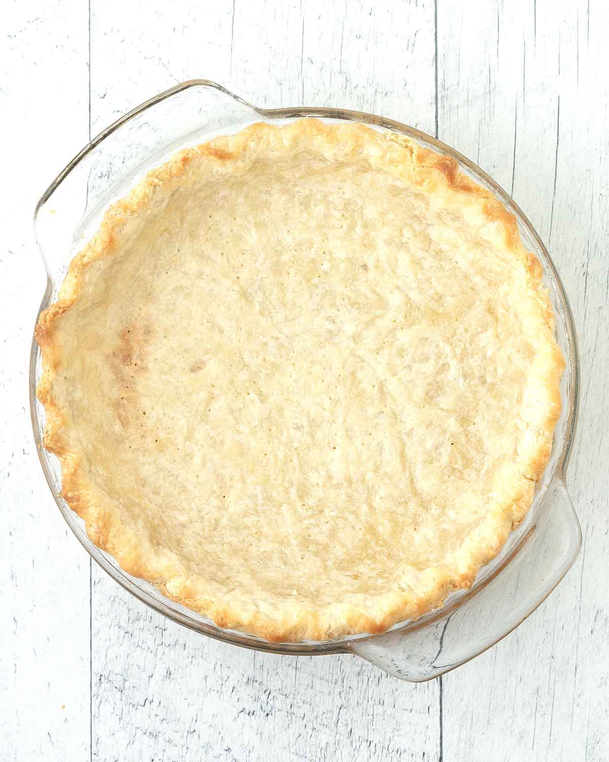 An overhead shot of a fully baked empty pie crust in a glass pie plate.