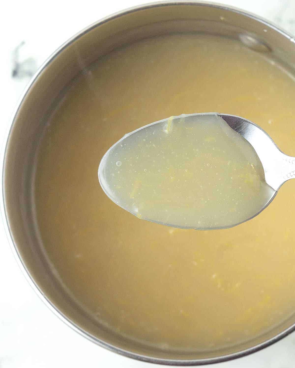 A spoon holding a small amount of vegan lemon curd above the pot it’s being prepared in.