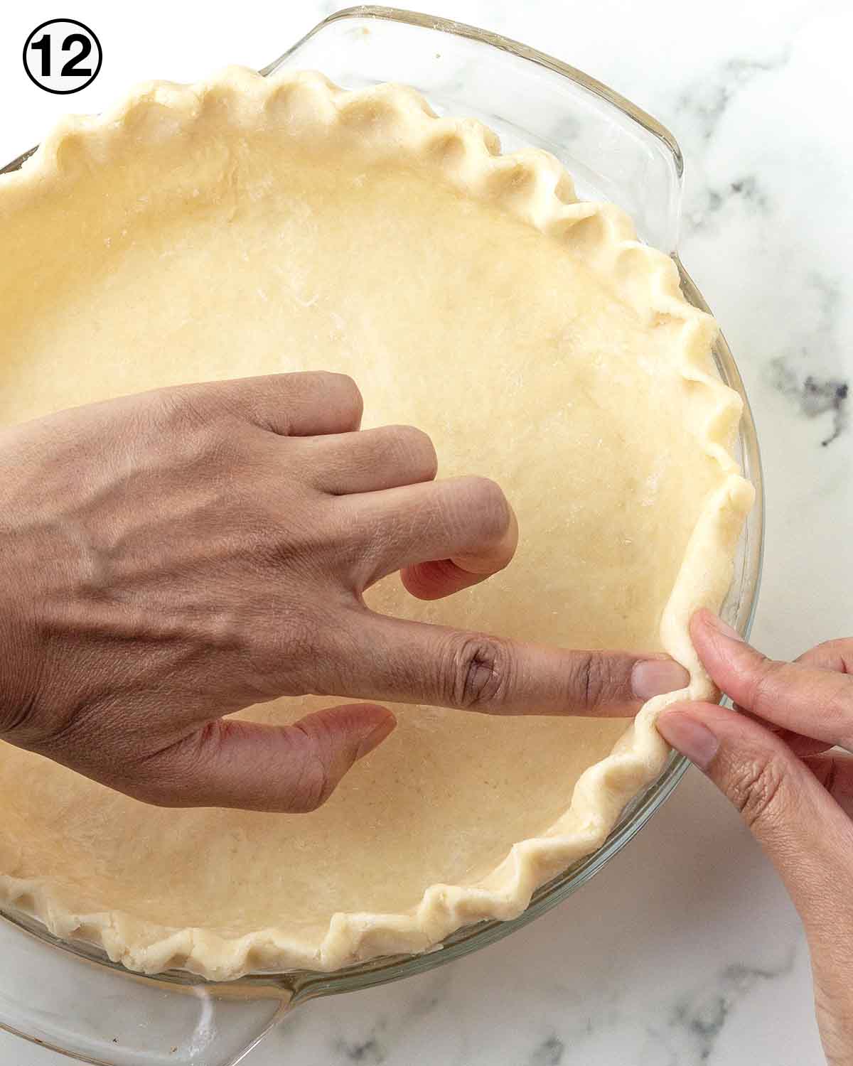 Hands crimping the edges of a pie crust.