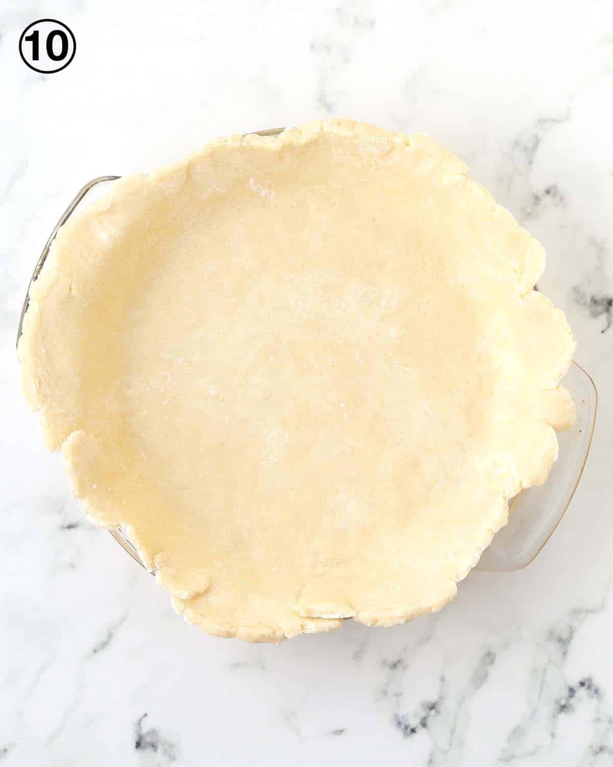 Raw, untrimmed pie dough in a glass pie dish.