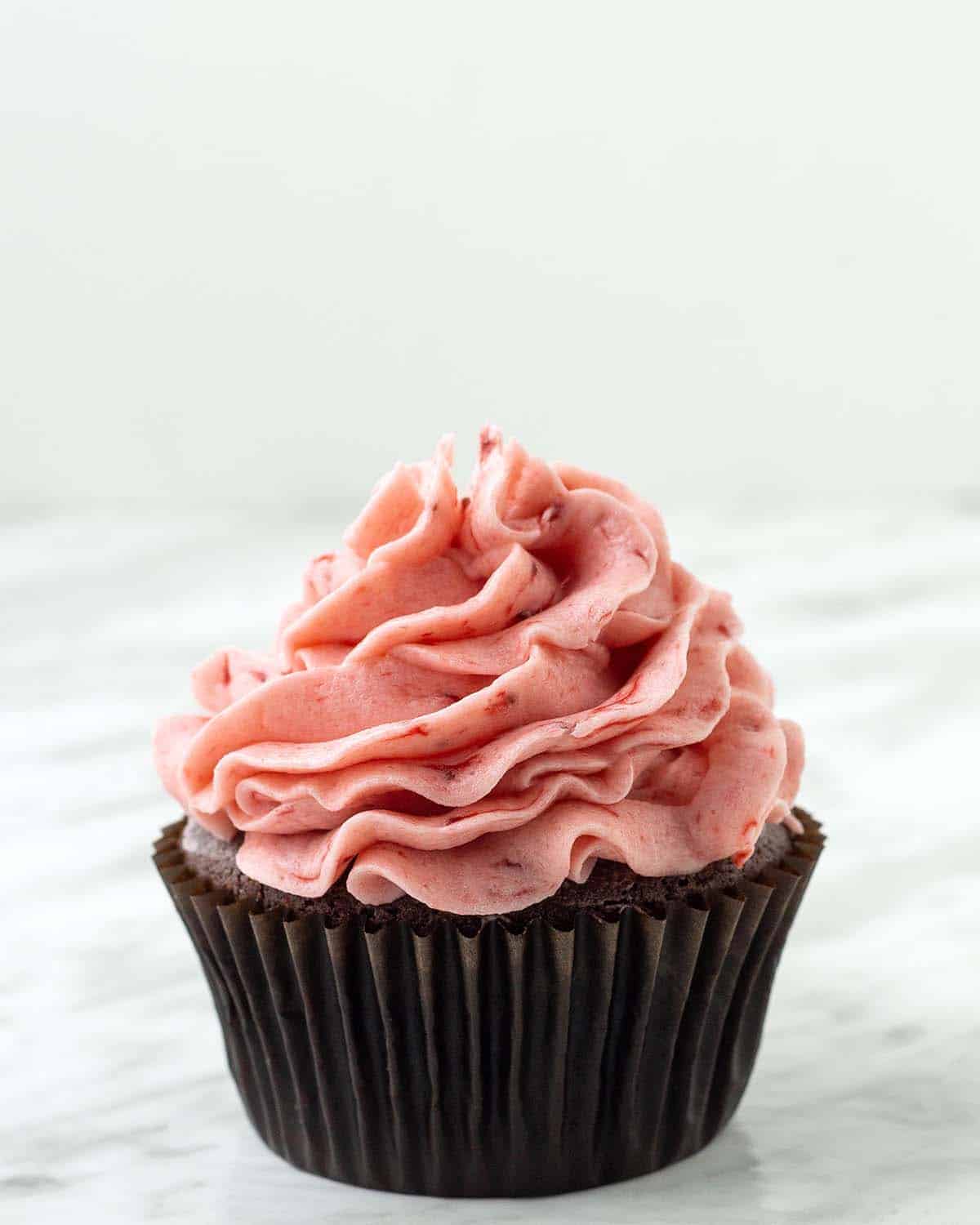 A chocolate cupcake topped with vegan strawberry frosting that was made with fresh strawberries.