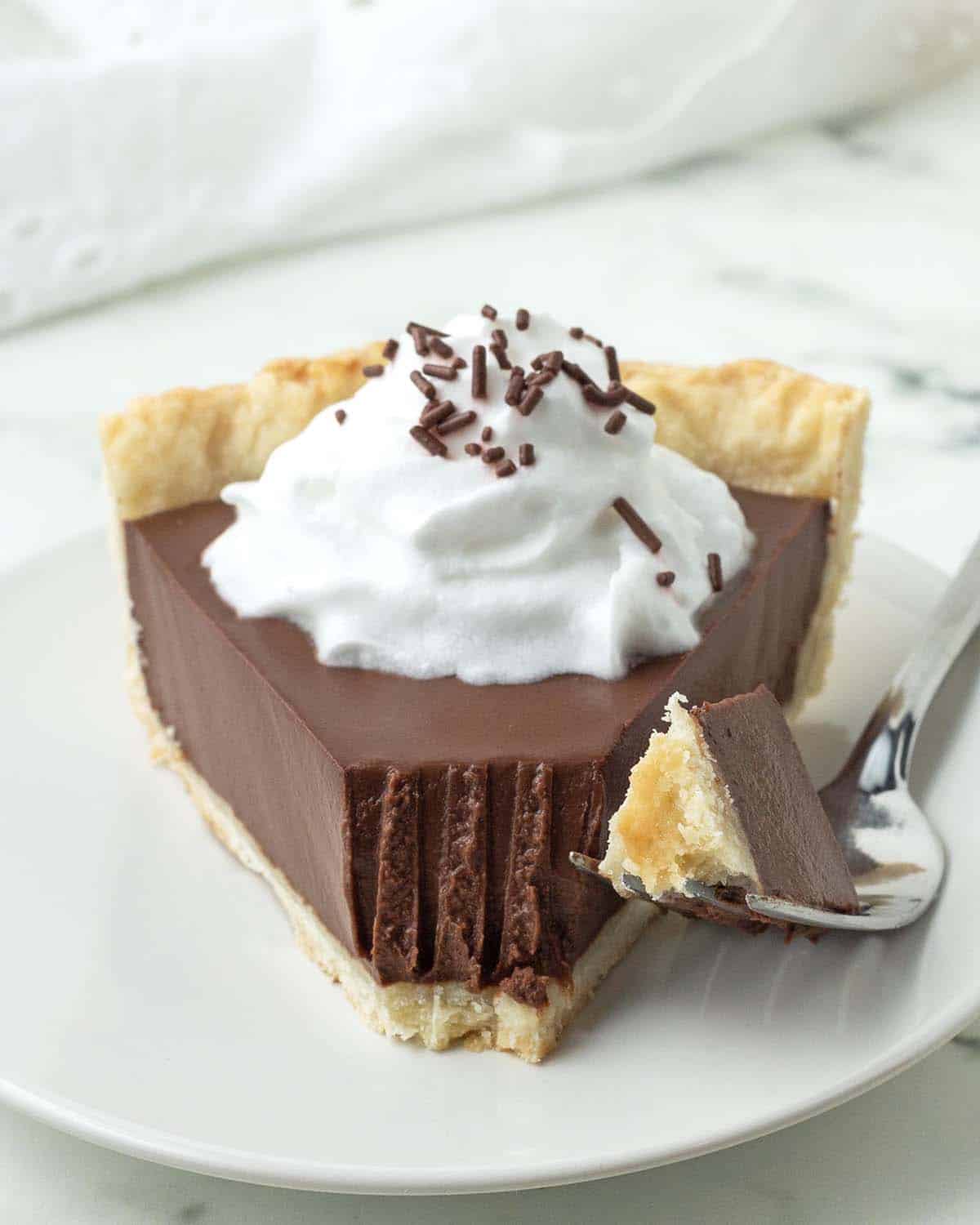 A slice of dairy-free vegan chocolate pie on a plate, a fork sits beside the slice with a piece of the pie on the fork.
