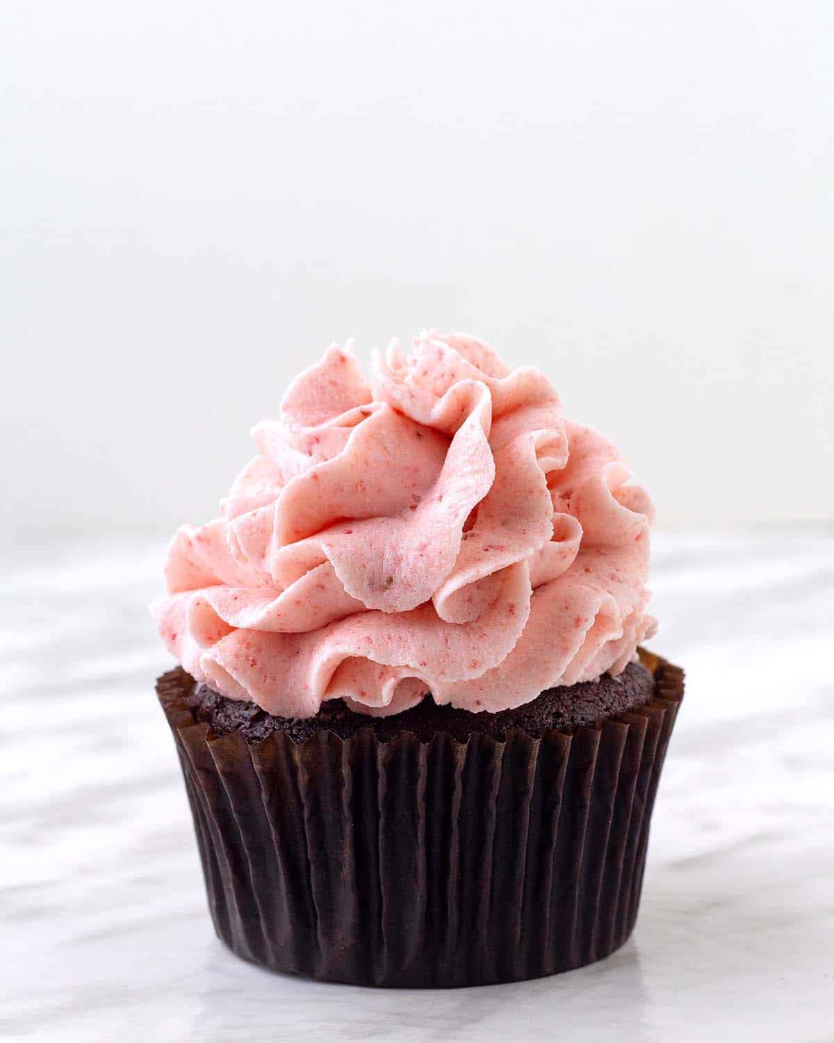 A chocolate cupcake topped with dairy-free strawberry frosting.