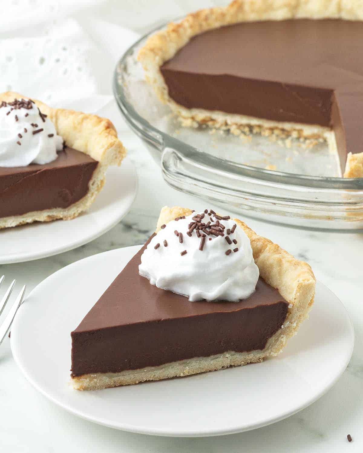 A slice of non-dairy chocolate pie on a white plate, and more pie sits in the background.