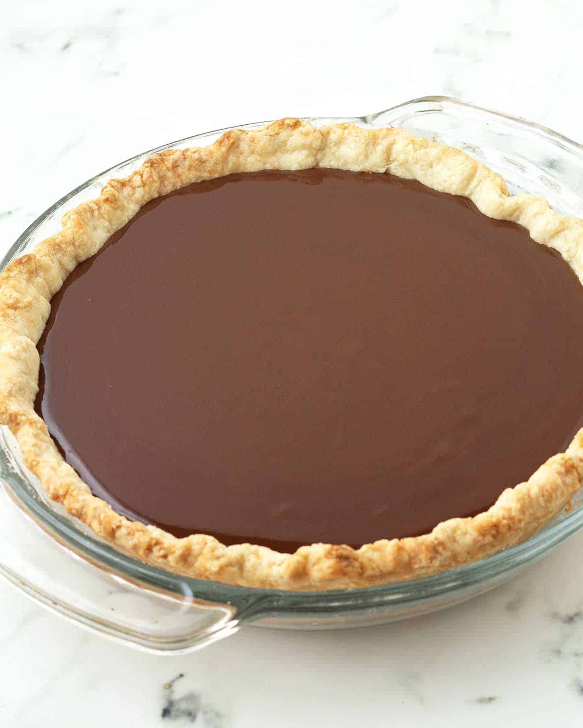 Chocolate pie filling sitting in a pre-baked pie crust, the filling is still liquid because it has not been chilled yet.