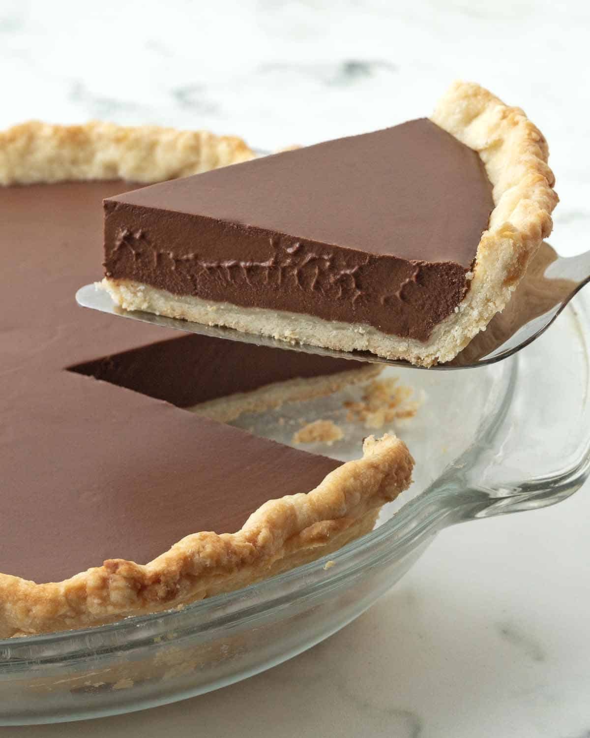 A slice of silky vegan chocolate pie is lifted out of a pie plate and away from the rest of the pie with a pie server.