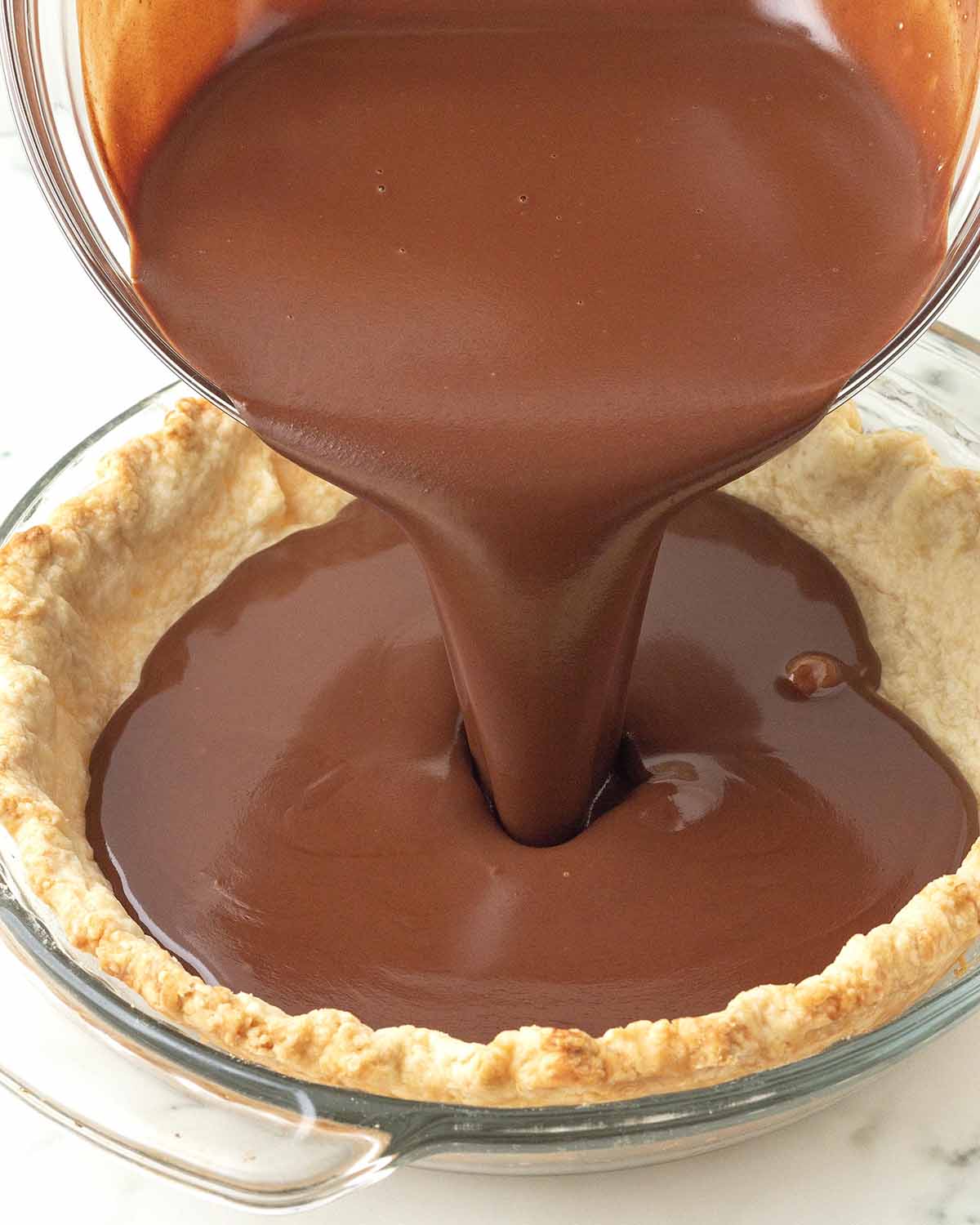 Vegan chocolate pie filling is being poured into a pre-baked pastry pie crust.