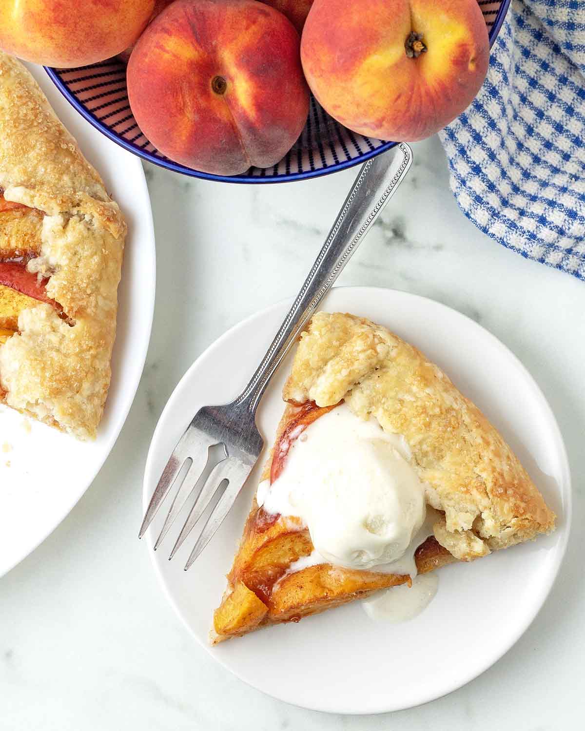 An overhead shot of a slice of peach galette, the slice is topped with ice cream that is melting.