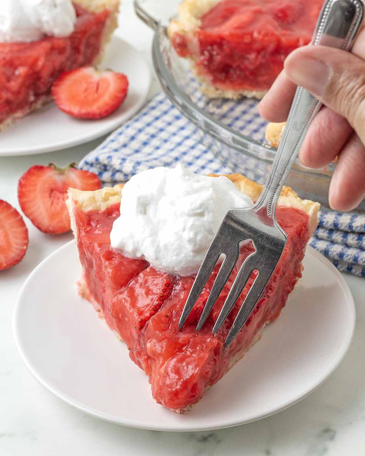 A fork taking a piece out of a slice of fresh strawberry pie.