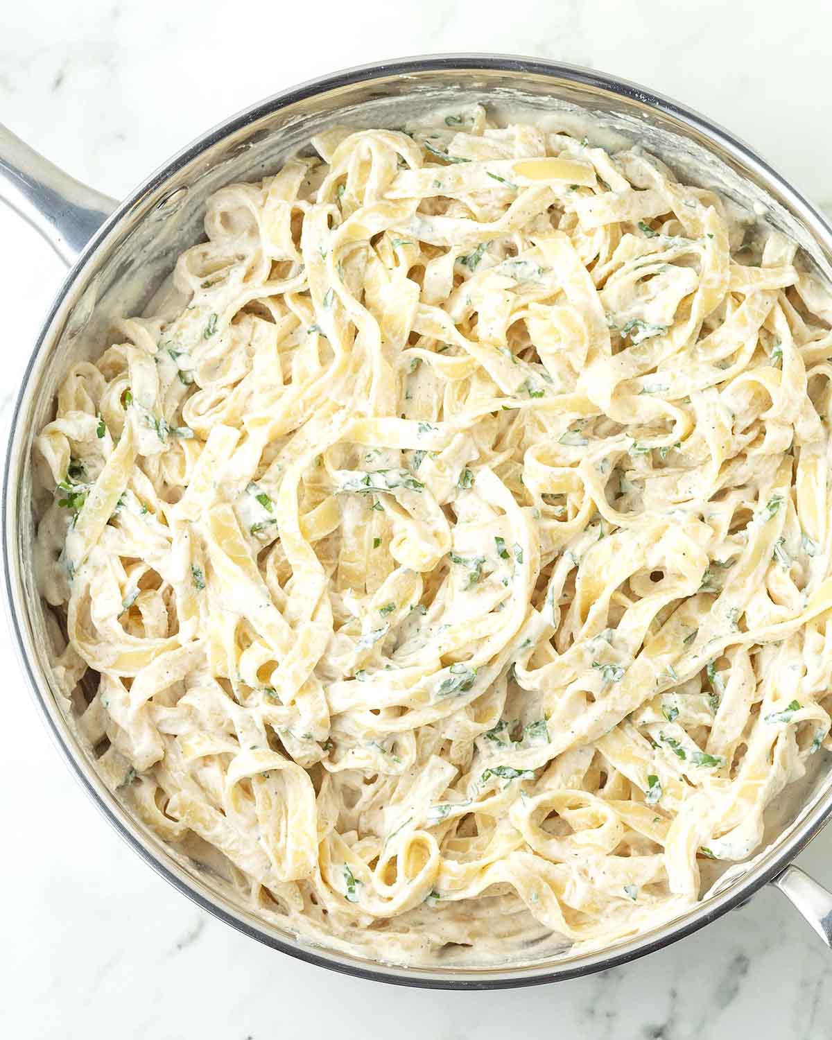 A large stainless-steel pan of freshly made tahini noodles, the pasta is garnished with fresh parsley.