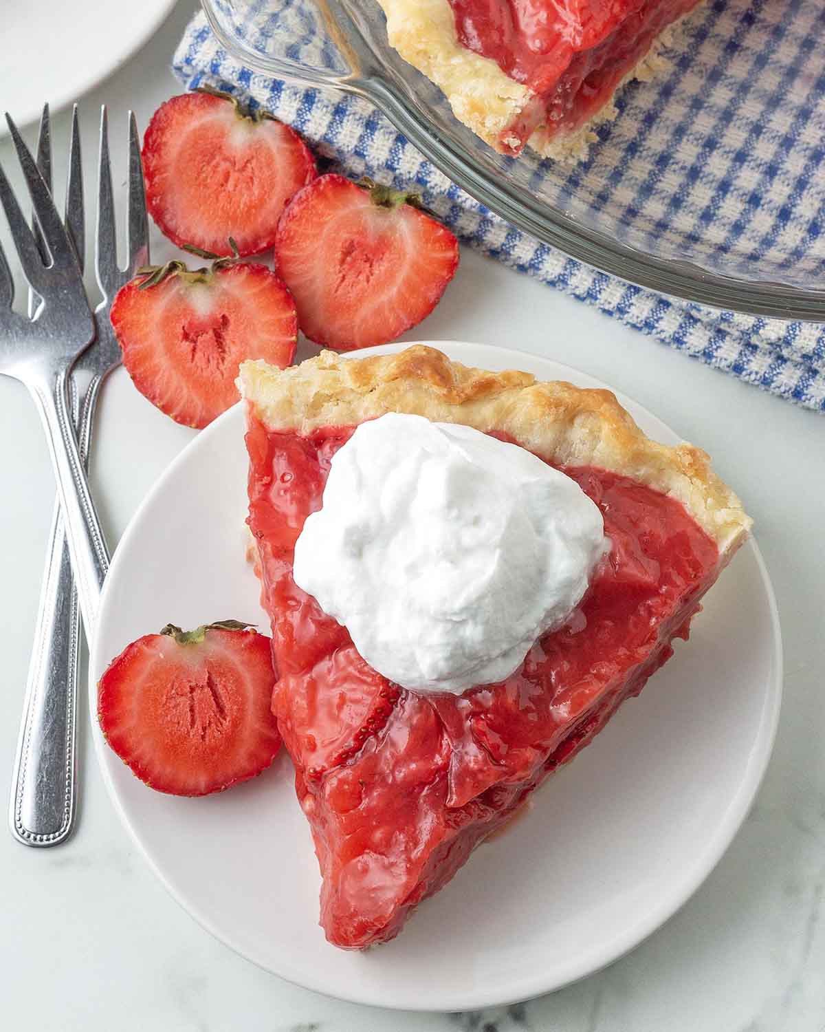 An overhead shot of a slice of strawberry pie on a white plate, the pie is topped with a dollop of dairy-free whipped cream.