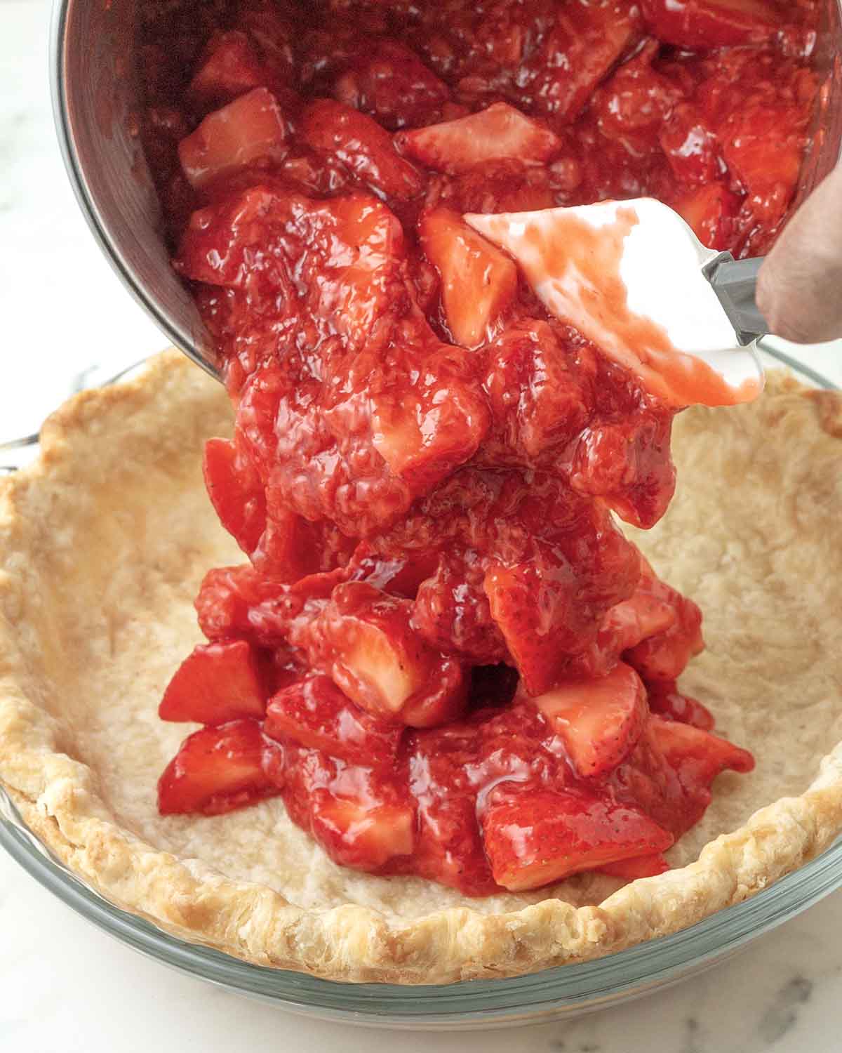 Vegan strawberry pie filling being poured into a pie crust.