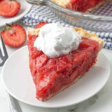 A close-up shot of a slice of fresh strawberry pie on a white plate.