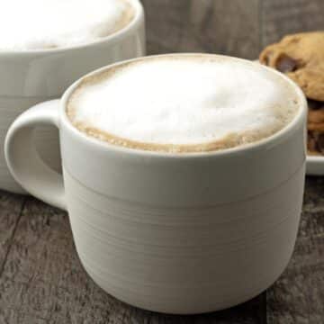 An almond milk latte in a white mug sitting on a dark wood table.