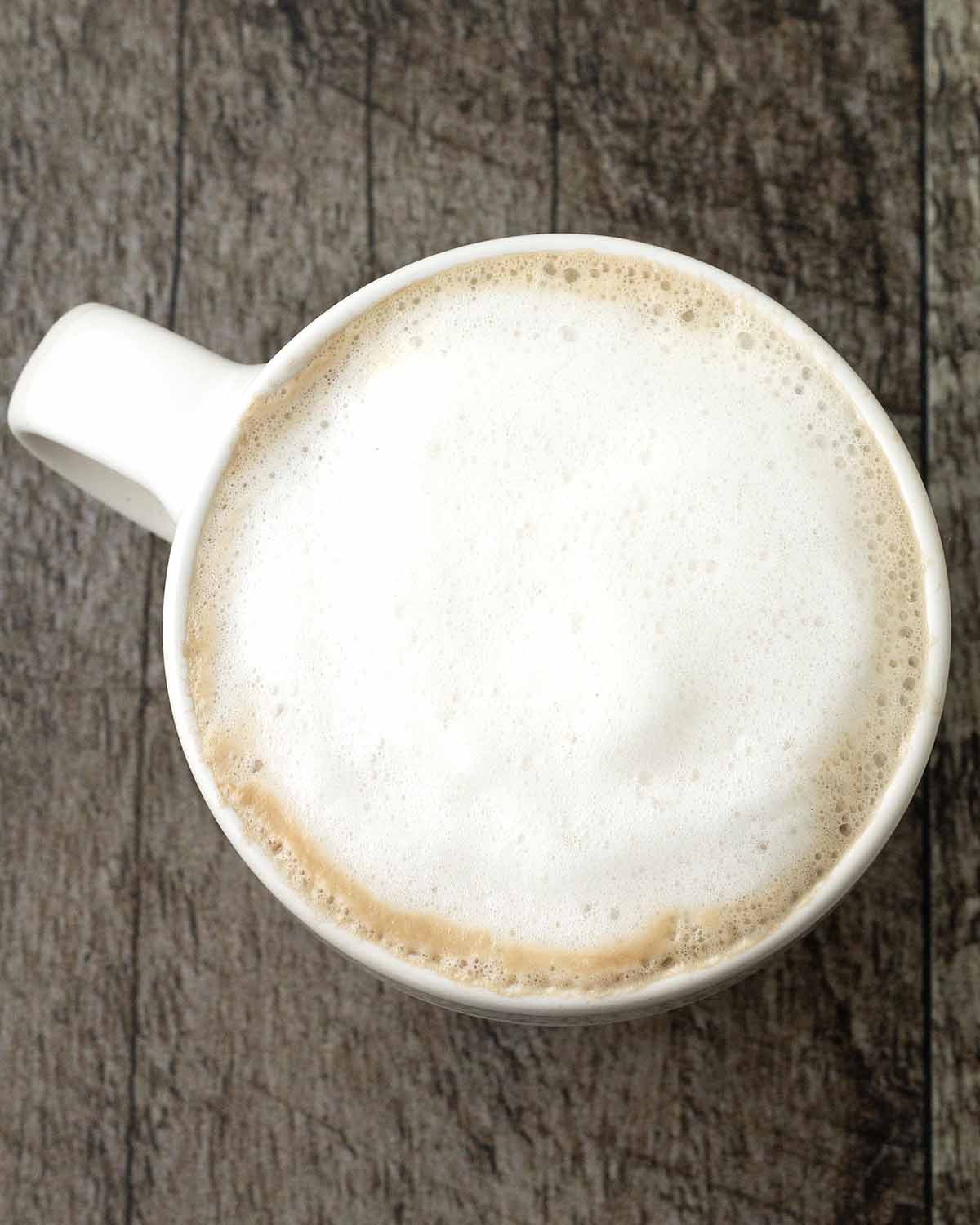 An overhead image of an almond milk latte topped with foam in a mug.