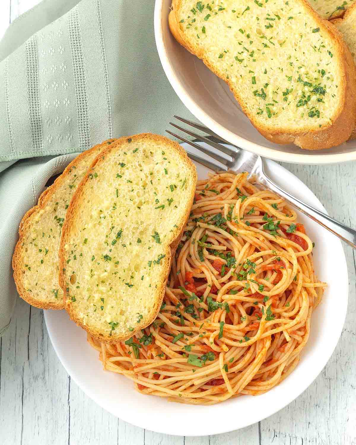 A plate of spaghetti with sauce, two pieces of garlic bread sit on the left side of the plate.