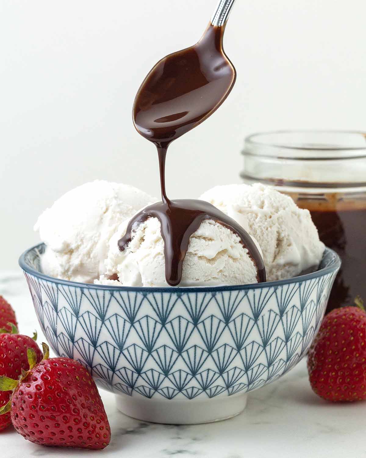Chocolate syrup being poured from a spoon onto coconut ice cream.