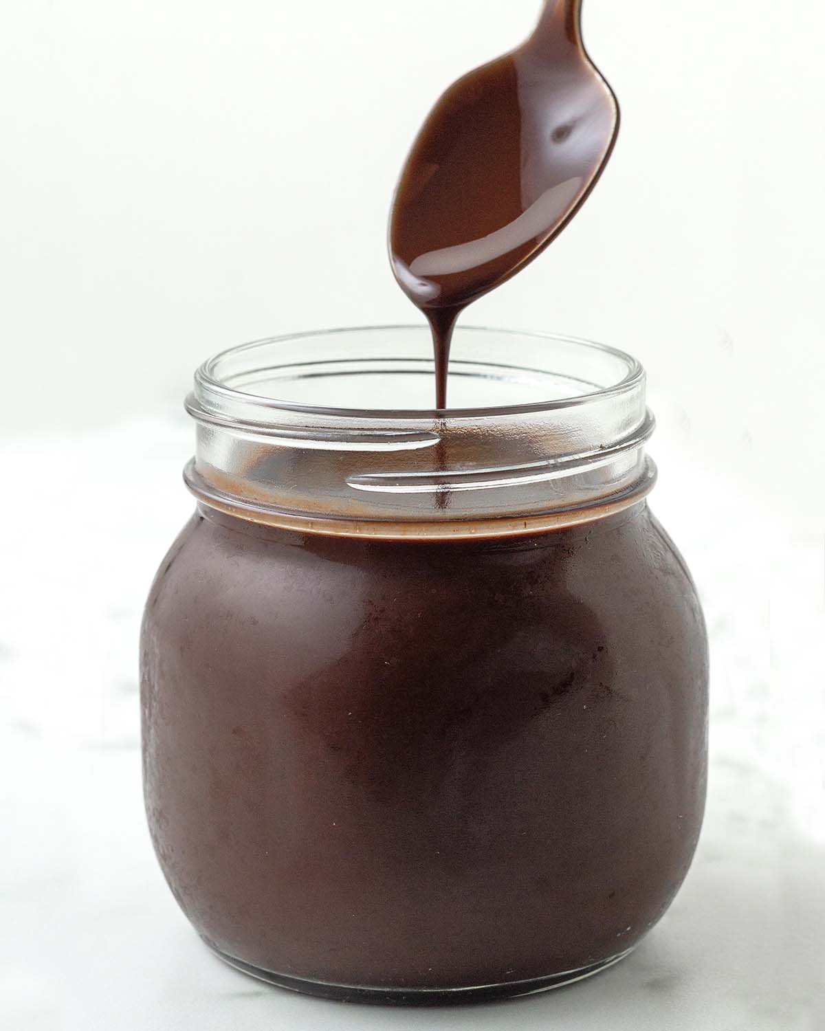 Chocolate syrup being poured from a spoon into a jar of more syrup.