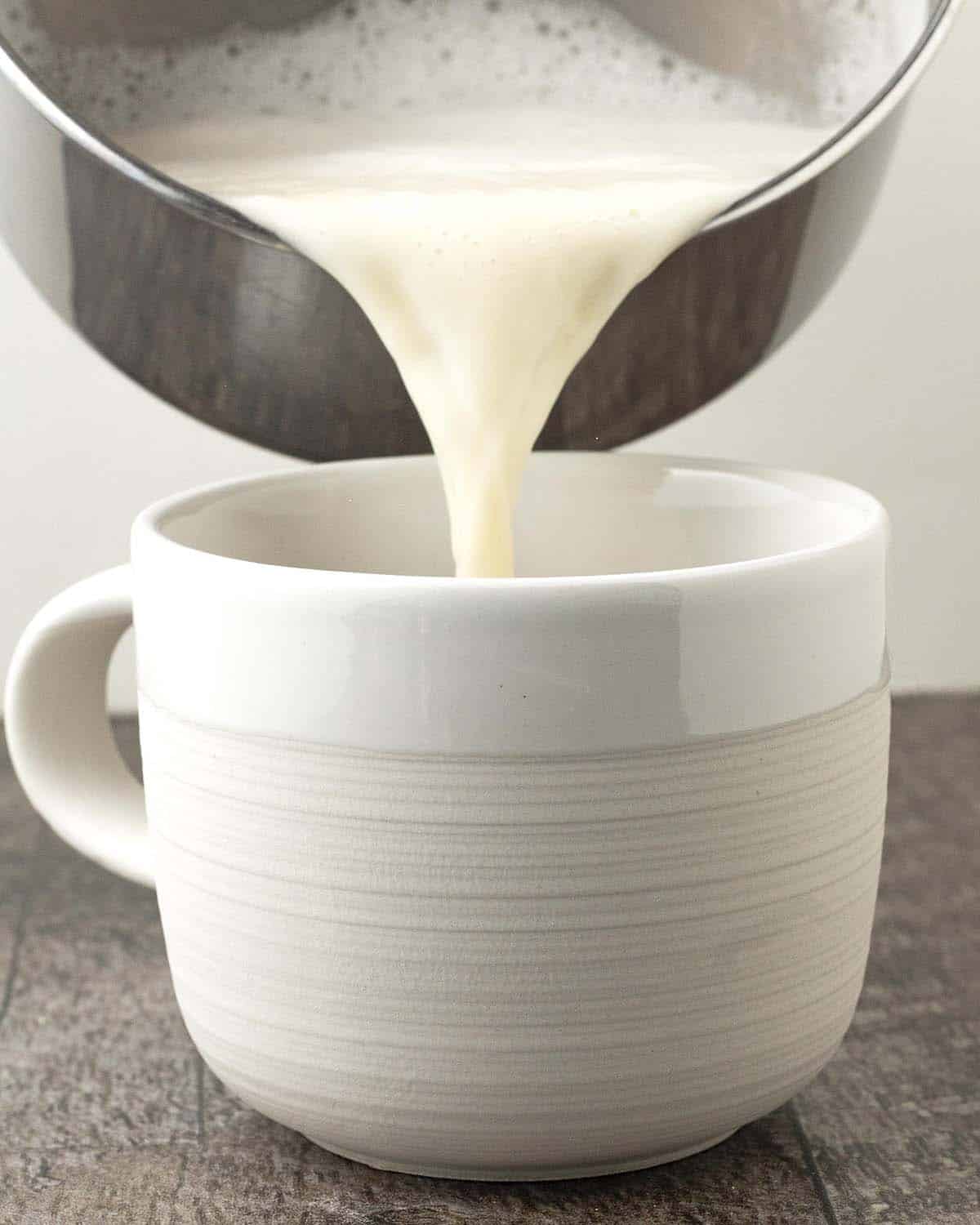 Almond milk being poured from a pot into a mug.