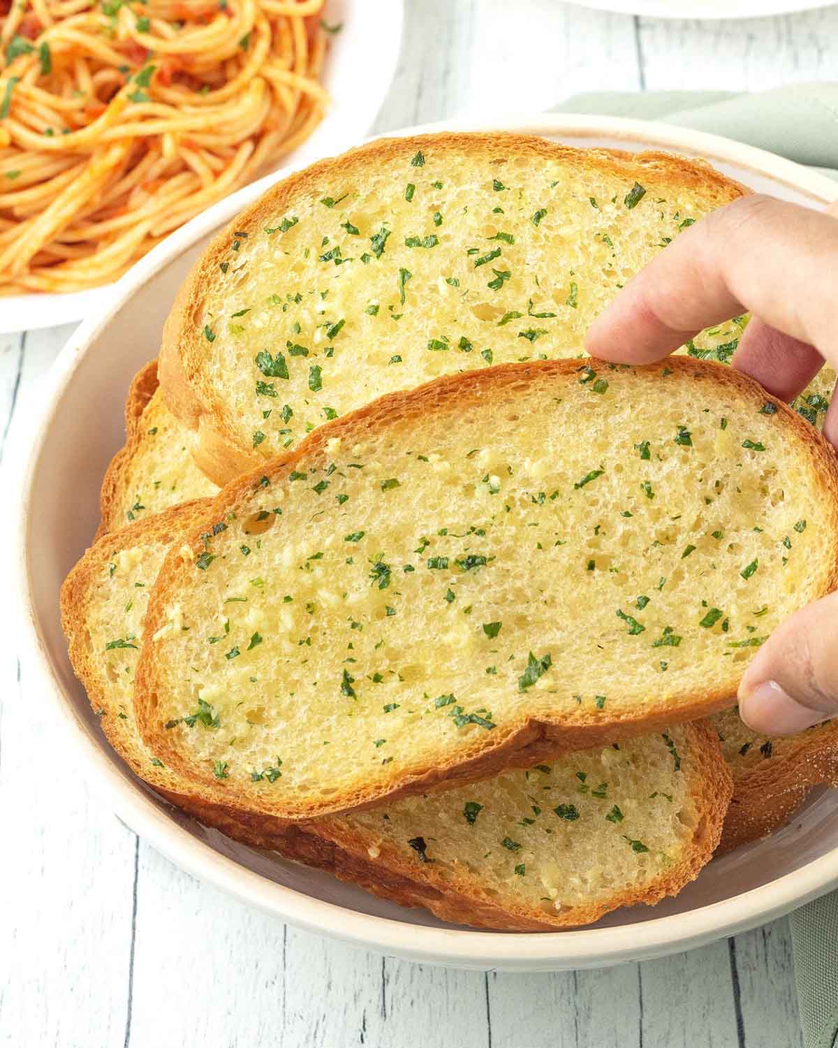 A hand taking a slice of garlic bread out of a dish.