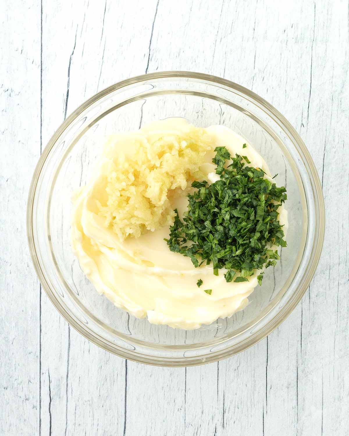 A small glass bowl filled with vegan margarine, chopped fresh parsley, and pressed garlic cloves.