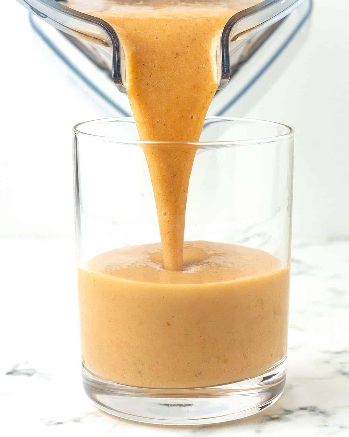 A freshly blended pumpkin spice smoothie bring poured into a glass.