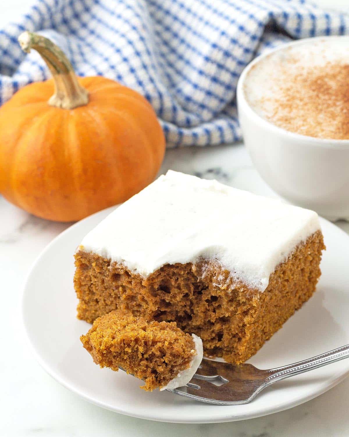 A vegan pumpkin spice bar on a white plate, a fork that has taken away a piece of the bar sits on the plate.