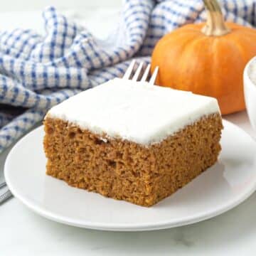 A pumpkin bar with cream cheese frosting sitting on a small white plate with a fork to the side.