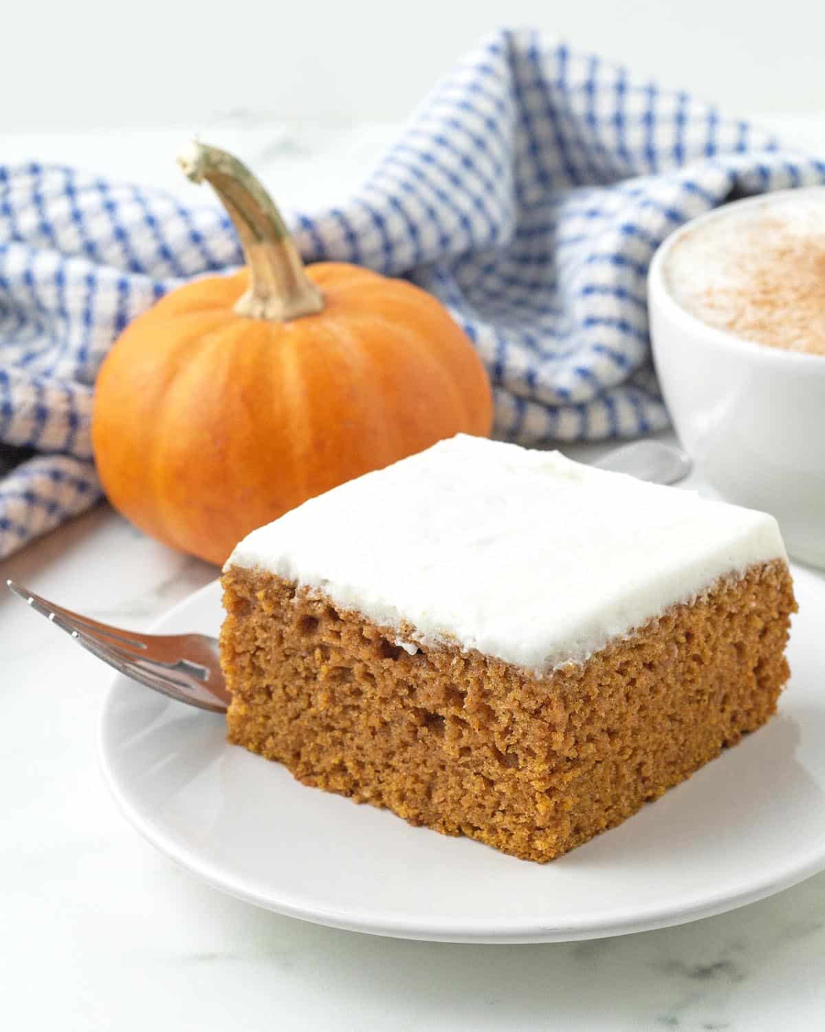 A square pumpkin bar with frosting sitting on a small white plate with a fork to the side.