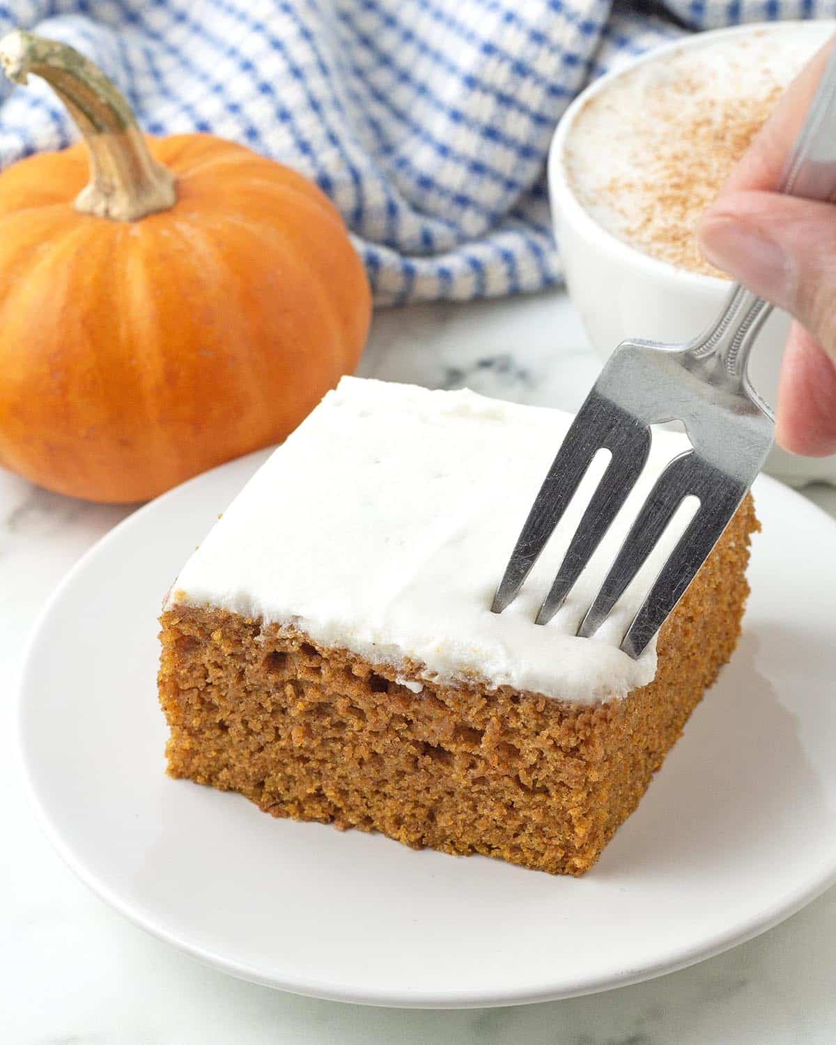 A hand holding a fork that is digging into a frosted vegan pumpkin bar.