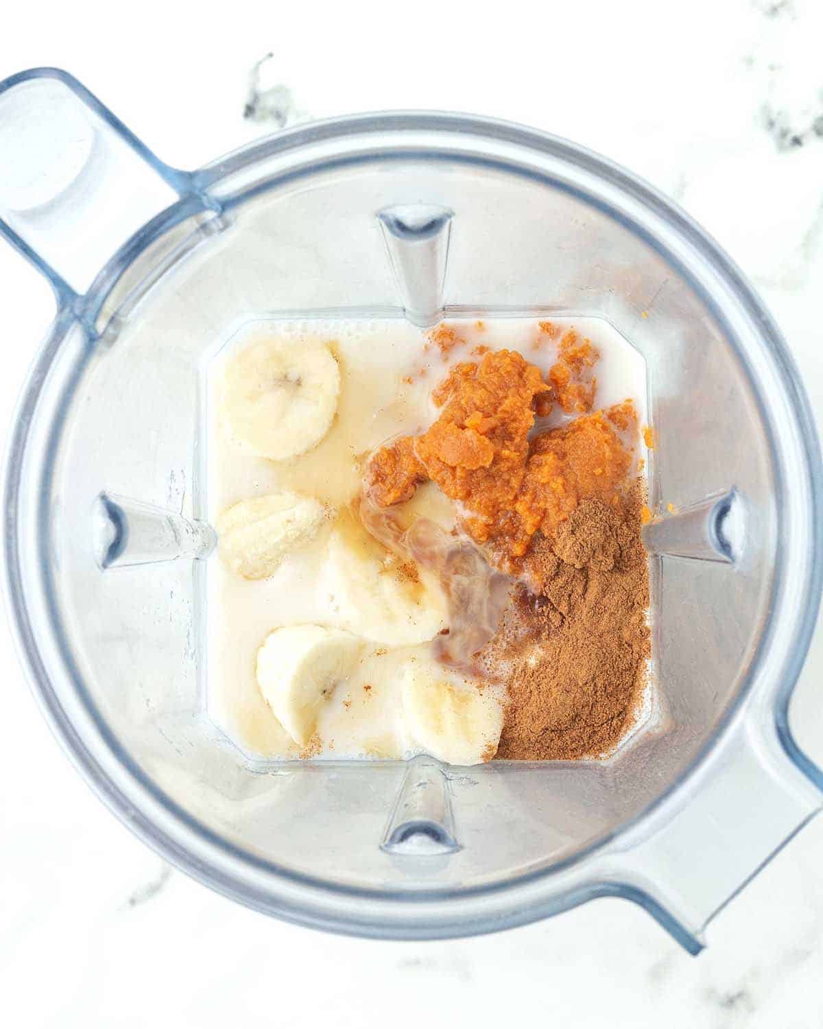 An overhead image showing the ingredients for a pumpkin pie smoothie in a blender canister just before being blended.