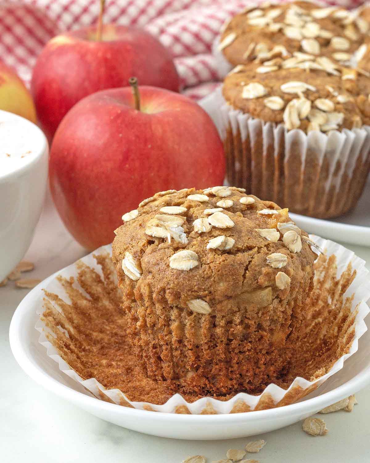 An apple cinnamon oatmeal muffin on a plate, the muffin wrapper has been peeled away.
