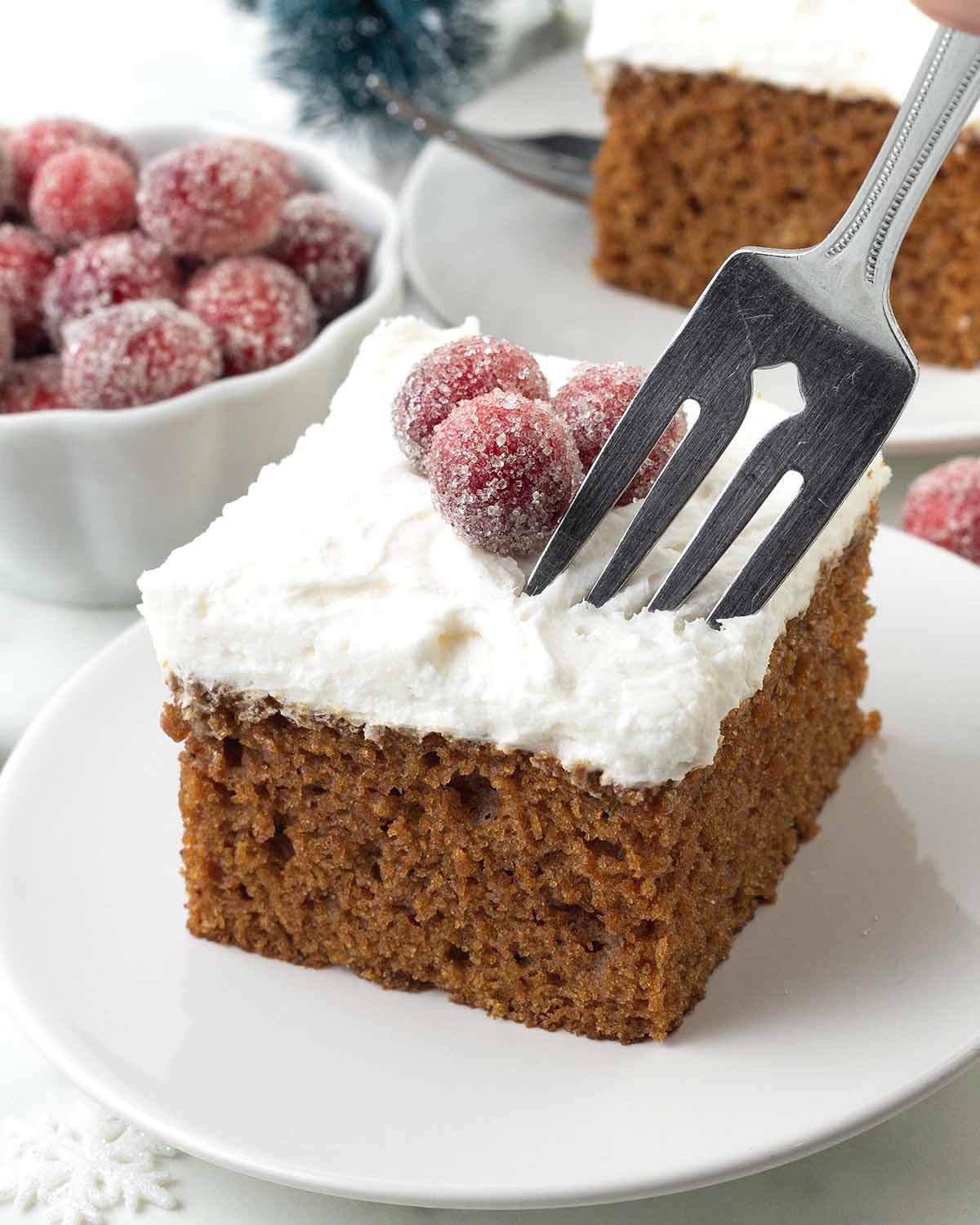 A hand holding a fork that is digging into a square of frosted vegan gingerbread cake.