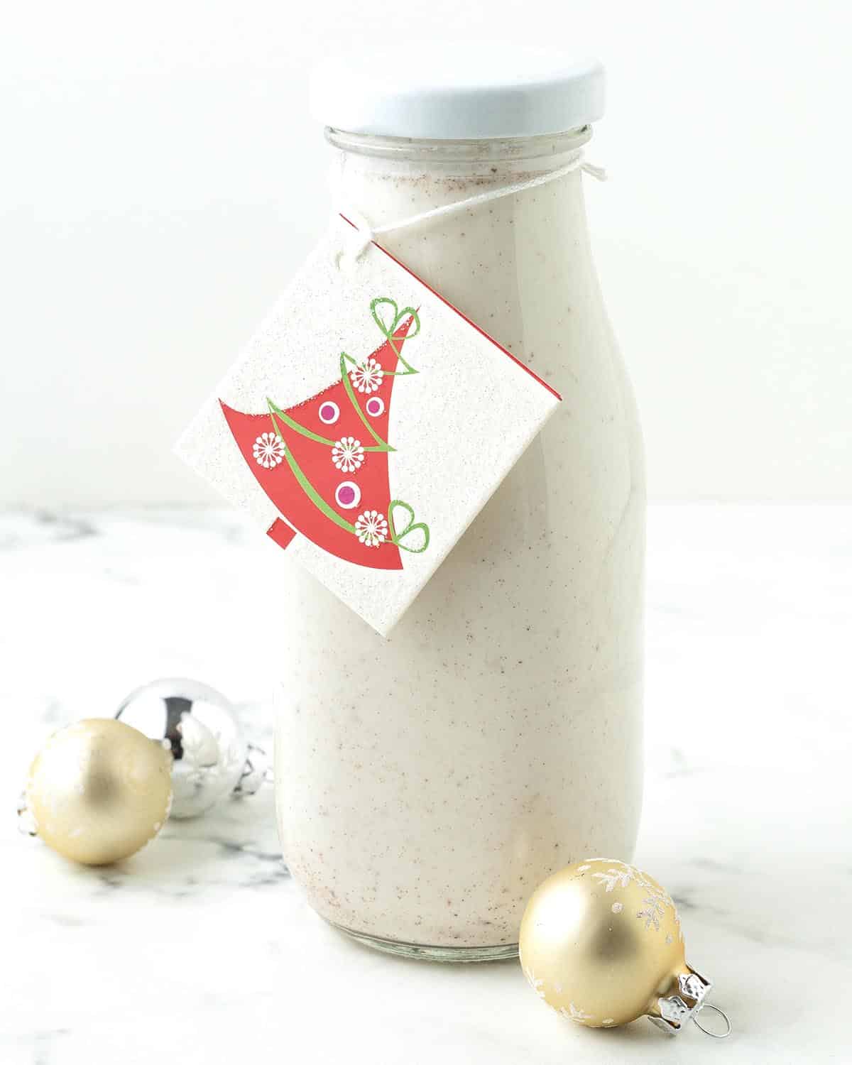A small glass bottle filled with non-dairy eggnog, the bottle has a holiday card tied around it.