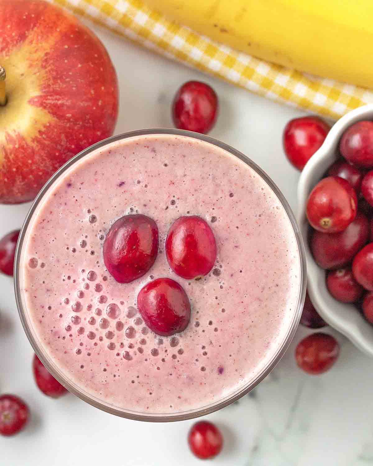 An overhead image of a cranberry apple banana smoothie in a glass.