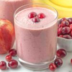 A glass filled with cranberry apple smoothie, the smoothie is topped with three fresh cranberries.