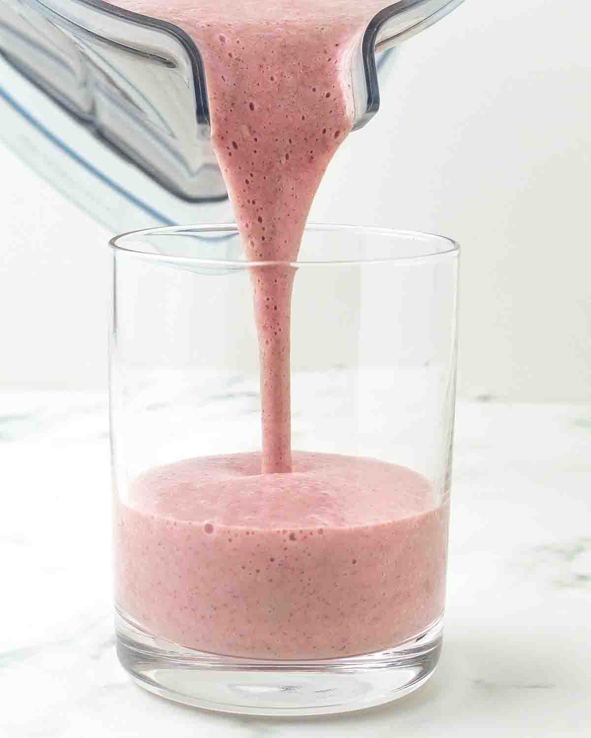 A freshly blended dairy-free cranberry apple smoothie being poured into a glass.
