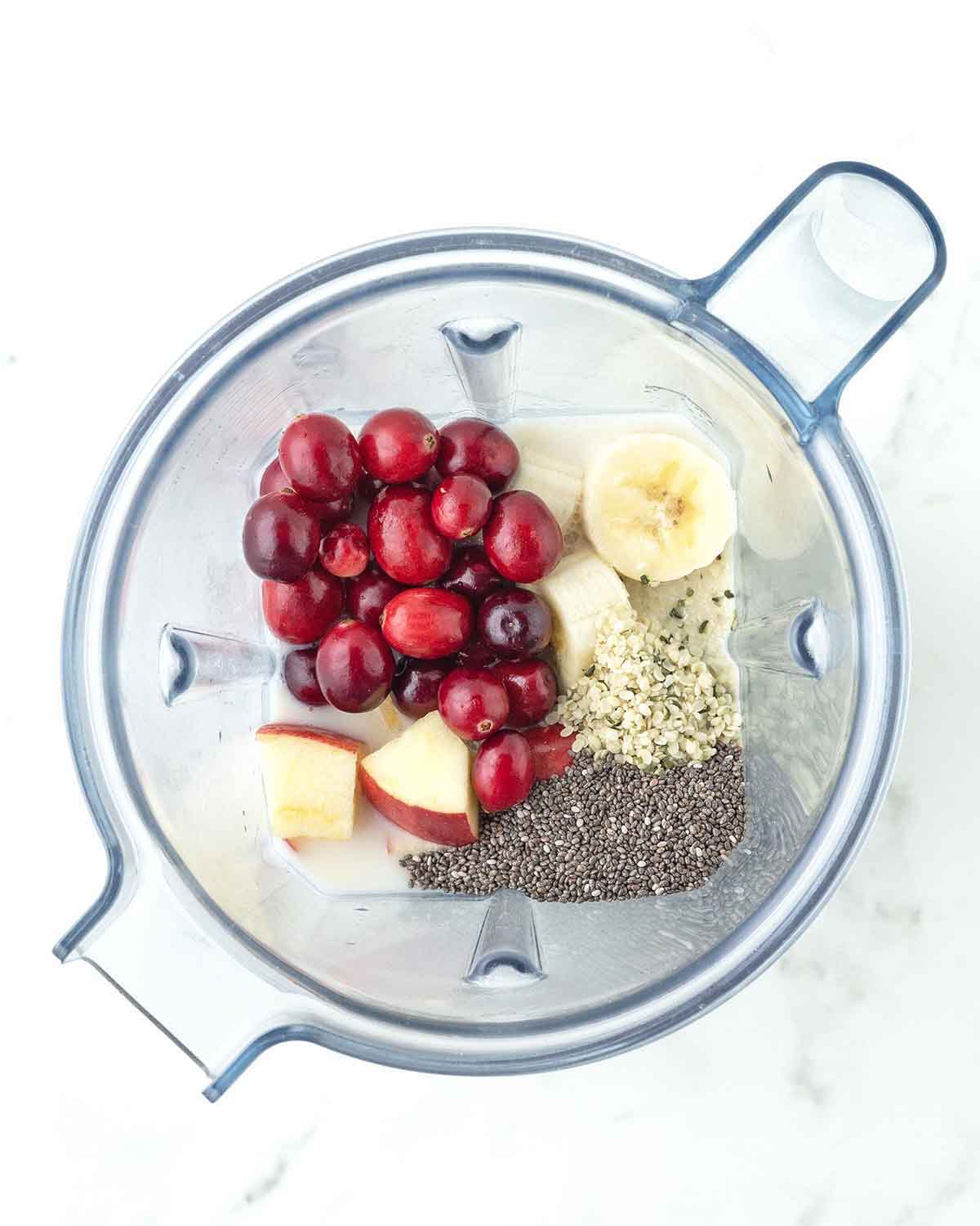 An overhead image showing the ingredients for a cranberry apple smoothie in a blender canister just before being blended.