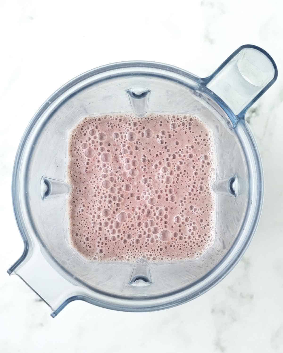 An overhead image of freshly blended cranberry smoothie in a blender canister.