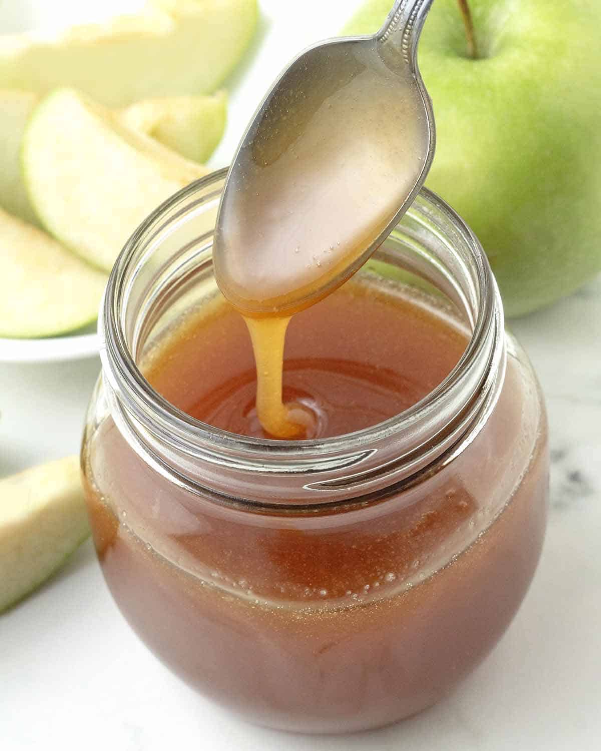 A spoon dripping with creamy vegan maple caramel sauce after being dipped into a jar of the sauce.
