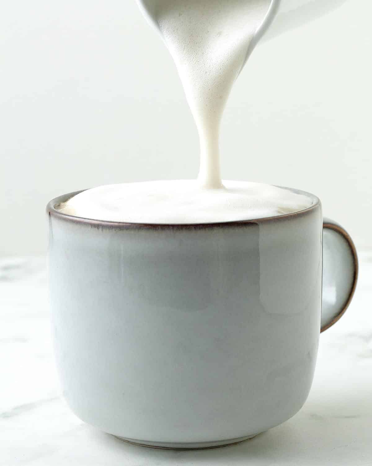 Foamed milk being poured on top of a chai latte in a mug.