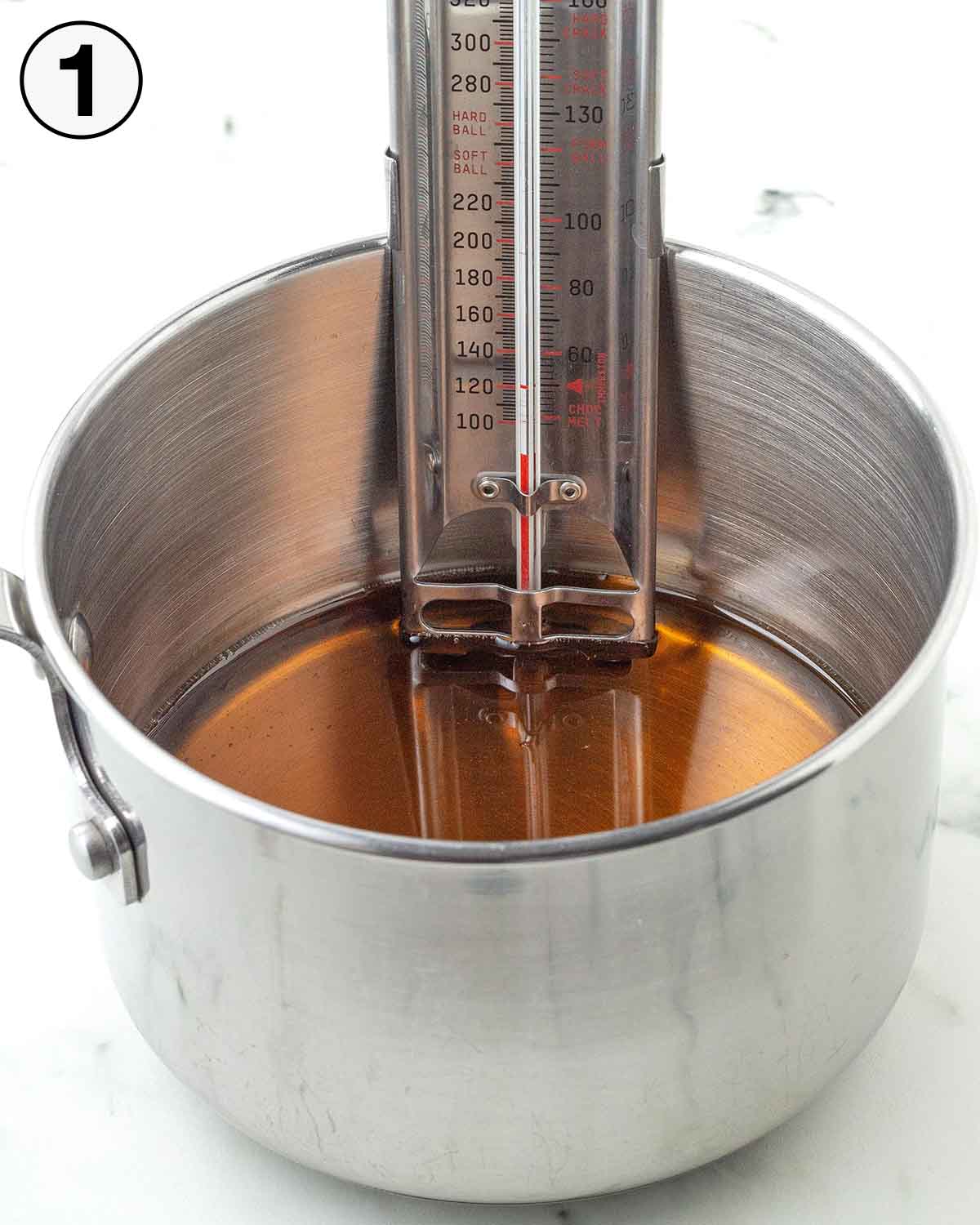 A candy thermometer in a pot of cold maple syrup.