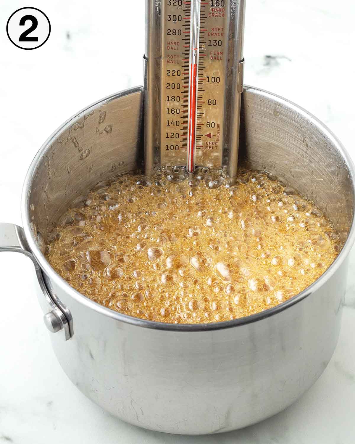 A candy thermometer in a pot of bubbling maple syrup.